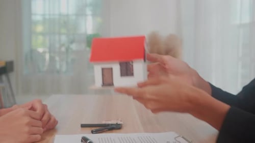 Closeup hands of young realtor woman real estate giving house model to hands customer man.