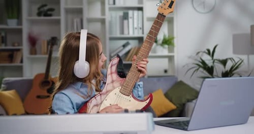 Young Girl Plays Guitar and Uses Laptop at Home