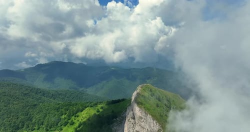 Flying trough white fluffy clouds above green mountain peaks. Beautiful summer sunny day on the high