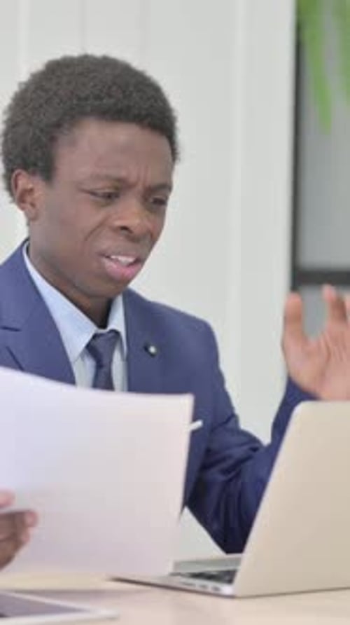 Young Man Working on Laptop and Holding Documents