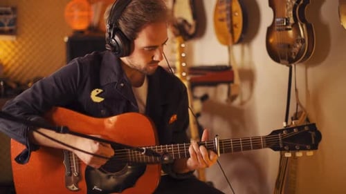 A young brunette musician man is learning how to play and record guitar music in a home recording st