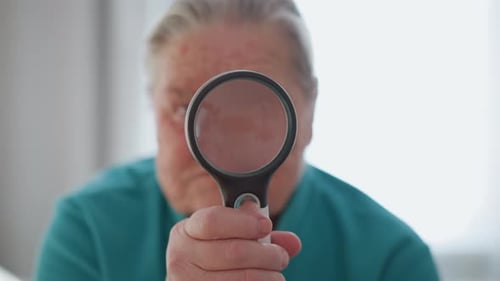 Senior Woman Holding Magnifying Glass Up To Eye