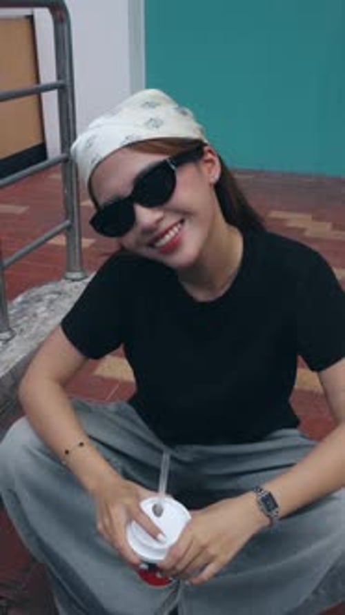 Smiling Woman with Drink Sits Outdoors in Portrait Shot
