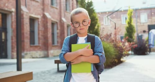 Portrait little boy holding books standing outside near school looking at camera and smiling. Joyful