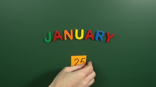 Hand sticking a sticker 25 January calendar day on school board. 25 date of January. Twenty fifth