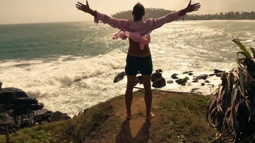 Young man stands with open arms enjoying summer vacation view of the ocean
