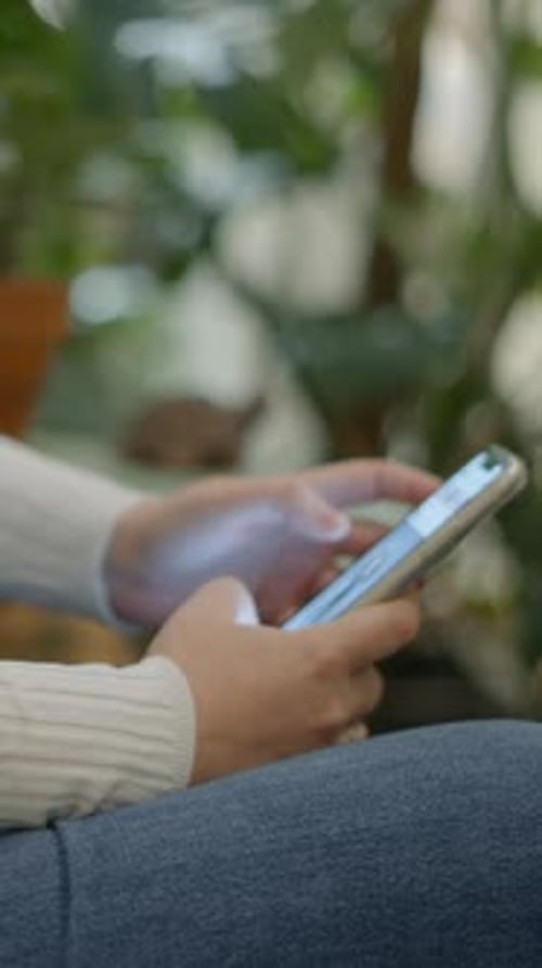 Unrecognizable Woman Using a Mobile Phone While Sitting on a Chair Side View