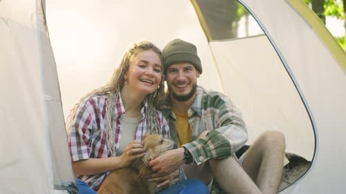 A Couple in Love Enjoys Relaxing in a Tent in the Forest While Their Playful Chihuahua Dog Rests at
