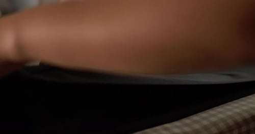 Slow motion close-up shot of an individual pressing a pair of pants using an electric iron and an ir
