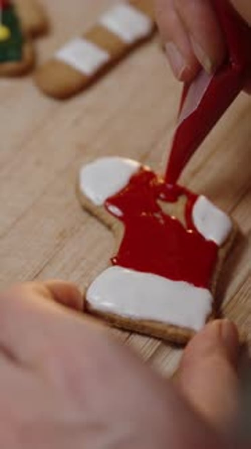 Vertical video. She Adds Red Icing to a White Stocking Cookie, Enhancing the Festive Look with Preci