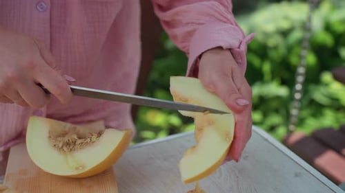 Cuisinier caucasien tranchant le melon mûr sur une planche de bois dans le jardin et la terrasse, couteau tranchant la peau et les graines