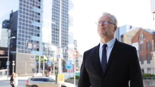 Business And People Concept - Senior Businessman Walking Along City Street And Checking Time On H...