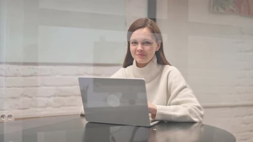 Woman Using Laptop at Table Smiles at Camera