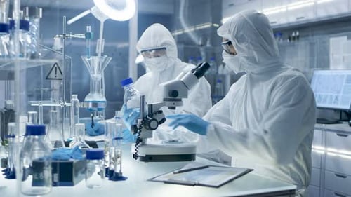 Scientists in protective suits using microscope in lab