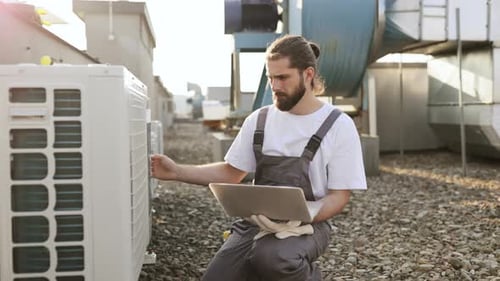 Technician Inspecting Air Conditioning Units With Laptop