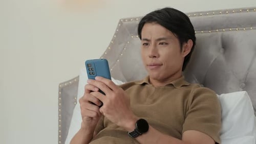 Young Restful Man with Smartphone Texting in Bed