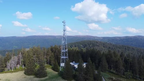Aerial orbit view around a tall telecommunication antenna mast pylon among mountain forest in Sérich