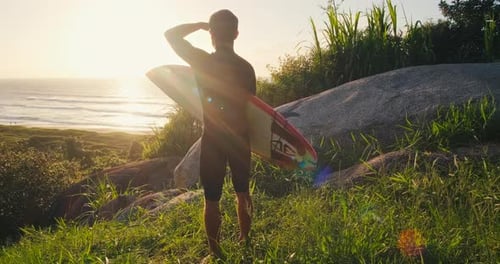 Surfer with board. Surfer in black wetsuit stands on the grass holds the surf board and checks the w