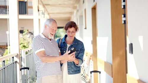 Senior Couple Outside Apartment on Holiday, Using Smartphone