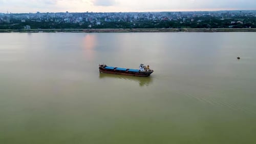 aerial view of small cargo ships traversing a river. The vessels create gentle ripples in the water,