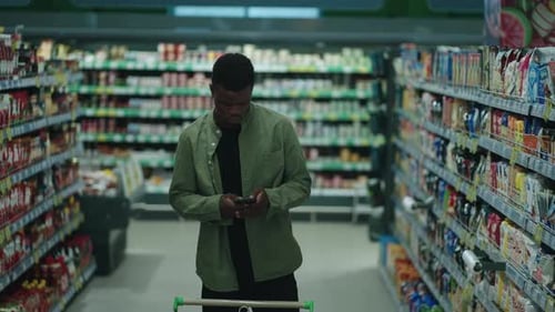 African American Man Shopping for Healthy Food in a Supermarket Using a Digital Device to Compare