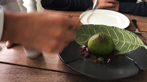 Waiter breaking sphere dessert cooked with lucuma ice cream, smoked cacao, carob and chocolate with