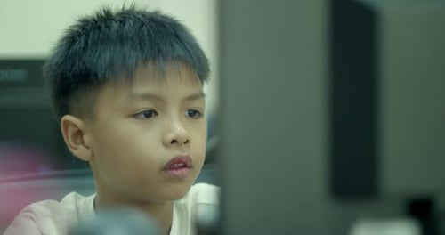 An Asian boy in elementary school is having fun using his desktop computer to play games
