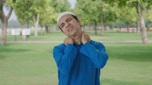 Sick Muslim man suffering from neck pain in park
