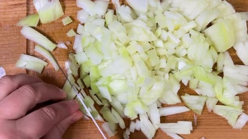 Cutting onions into small cubes with a knife on a wooden cutting board. Top view.