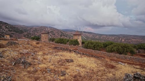 Windmills rise above dry hills in a remote, cloudy landscape