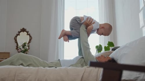 Happy mother holding baby high on bed indoors