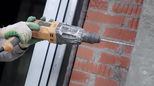 Hands of Worker Hold Drill While Penetrating Solid Wall