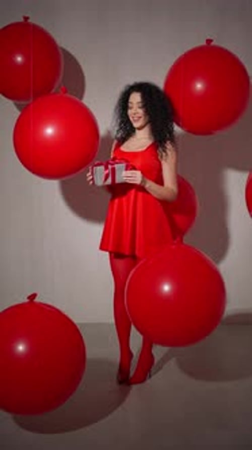 Smiling Woman in Red is Holding Gift Box Among Red Balloons