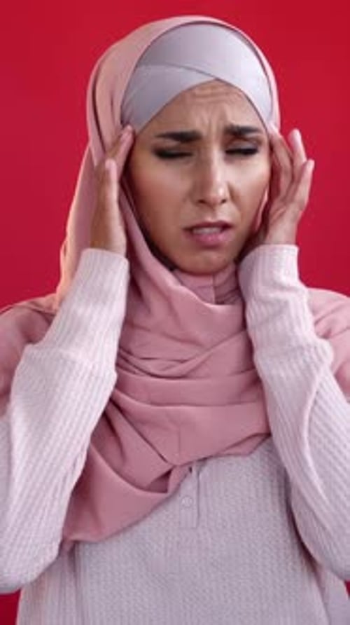 Woman With Headache Rubbing Temples on Red Background