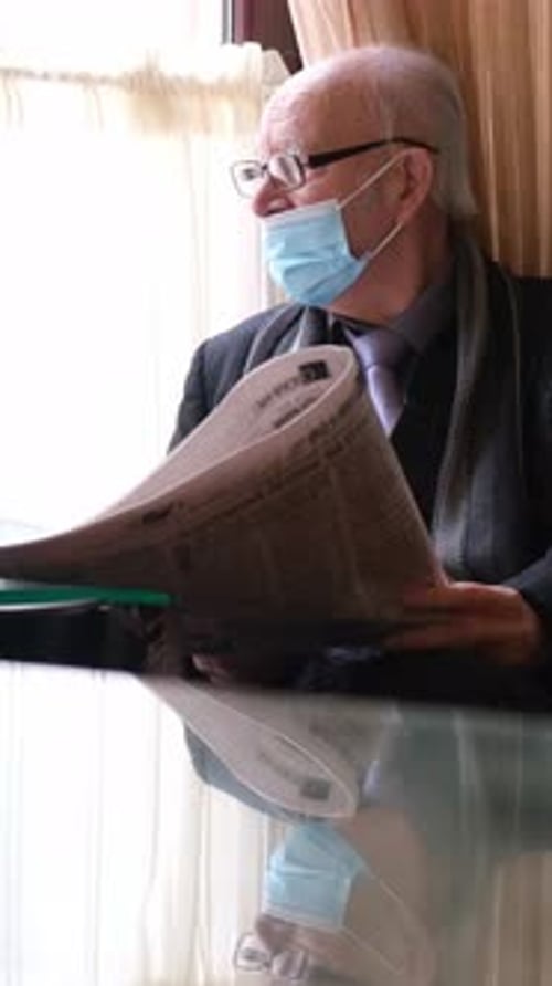 Senior Man Reading Newspaper at Home Wearing Mask