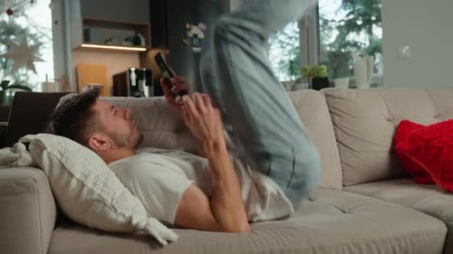 Young Man Lying on Sofa Using Phone