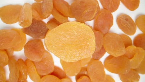 Top view, dried apricot rotates against the background of a heap of other dried apricots.