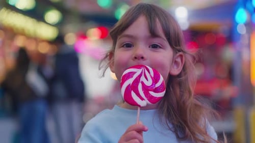 Child Enjoys Lollipop at a Brightly Lit Carnival