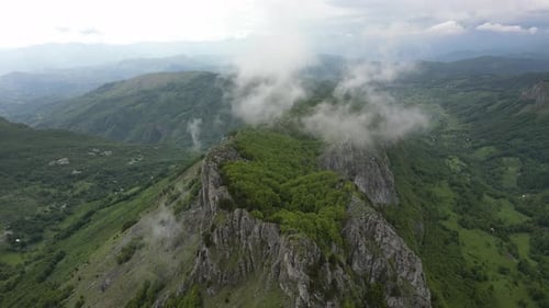 Flying over beautiful green mountains. In the background, stone cliffs with snow are visible.