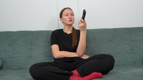 Woman Sits on Couch with Remote Control