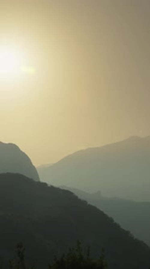 Vertical video. A Silhouette of a Person against the Backdrop of the Setting Sun behind the Mountain