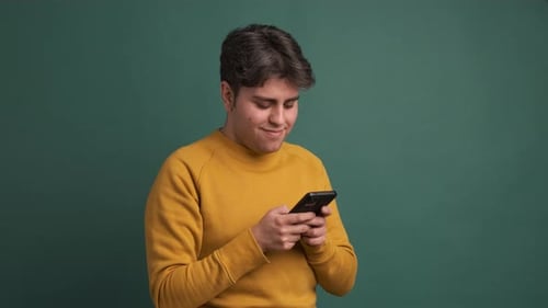 Happy Man Text Messaging Via Cellphone in Studio