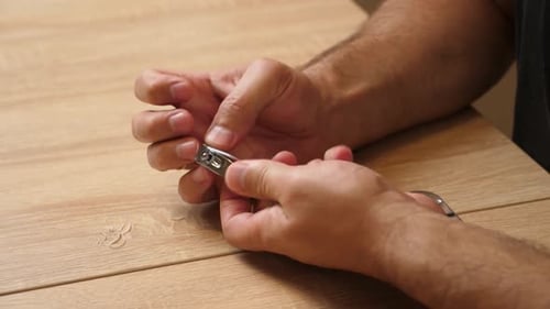 Man Clips His Fingernails at a Wooden Table