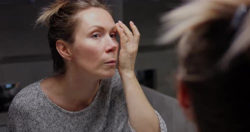 Woman Applies Cream to Face in Mirror
