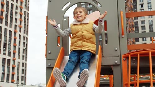 Cámara lenta de un niño feliz y alegre deslizándose por el tobogán en el nuevo patio de recreo