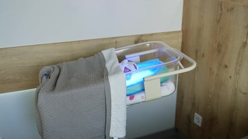 Transparent crib with newborn kid covered with blanket.