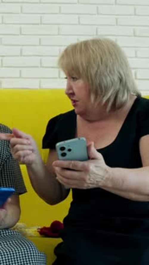 Two Senior Women Using Smartphones on Yellow Couch
