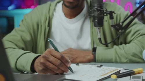 Adult Writes Notes Next to Microphone and Laptop