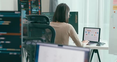 Woman Coding Software at Desk with Multiple Monitors