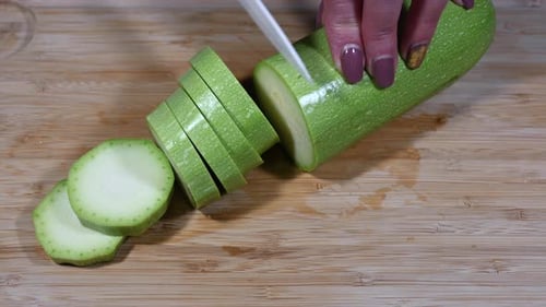 Zucchini Being Sliced on Wooden Cutting Board